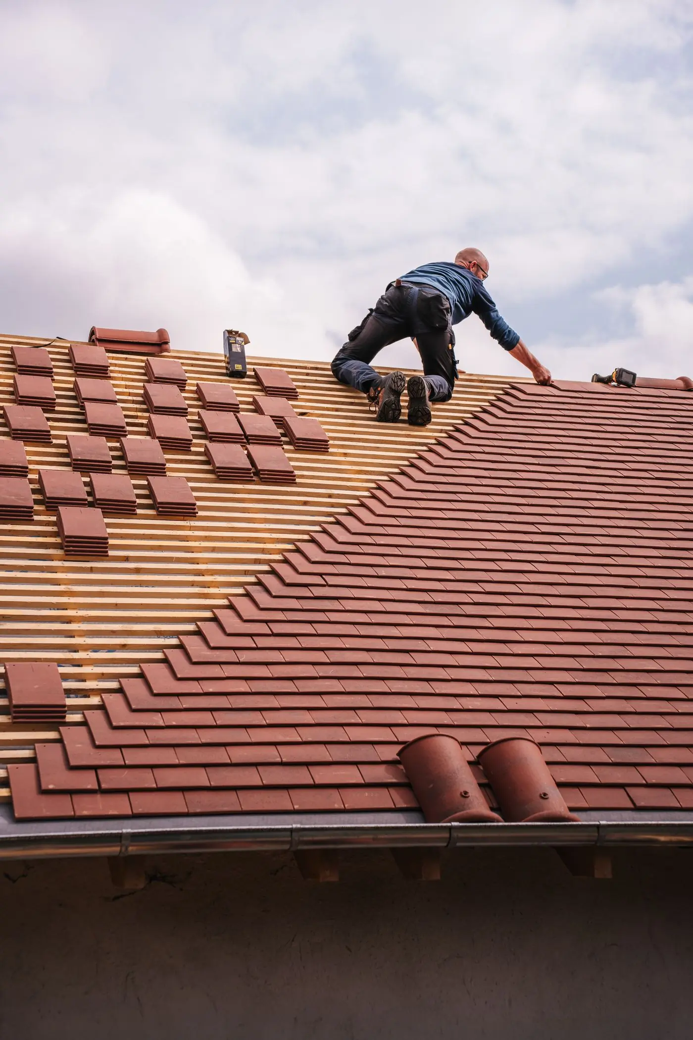 A roofer setting clay tiles on a newly battened slope