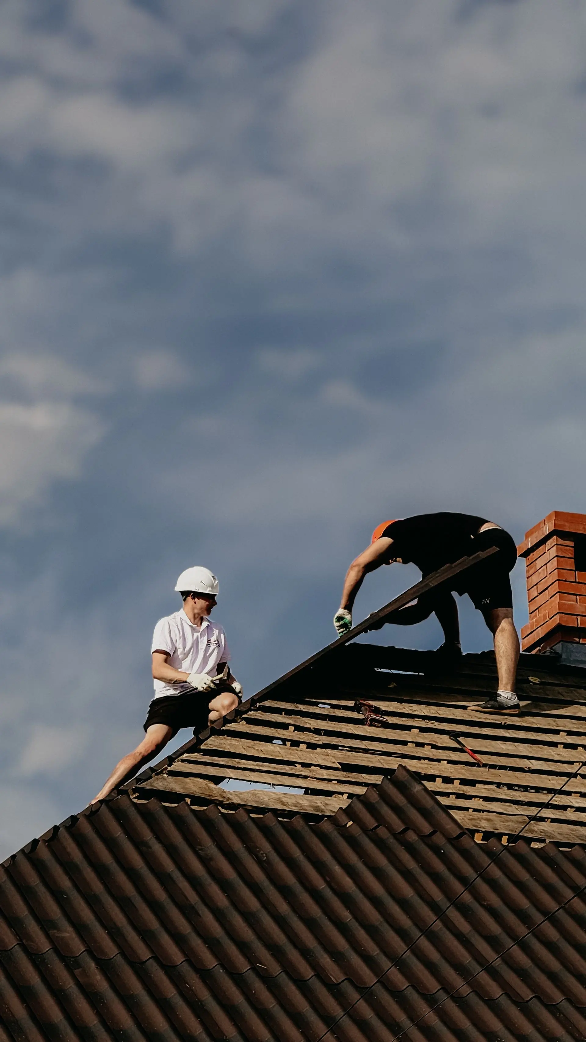 Two roofers stripping an old covering under a heavy sky