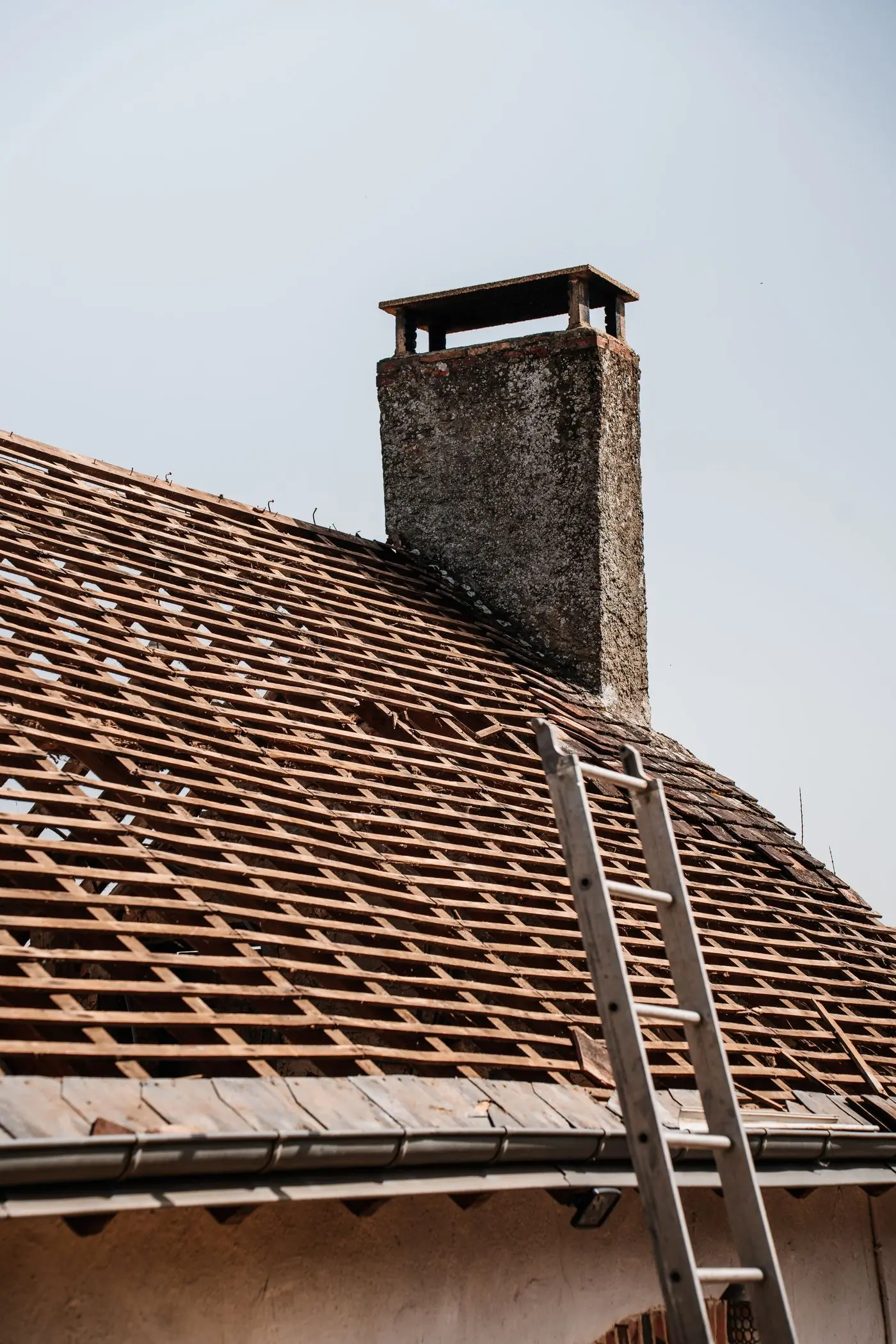 A roof stripped back to the battens around a brick chimney