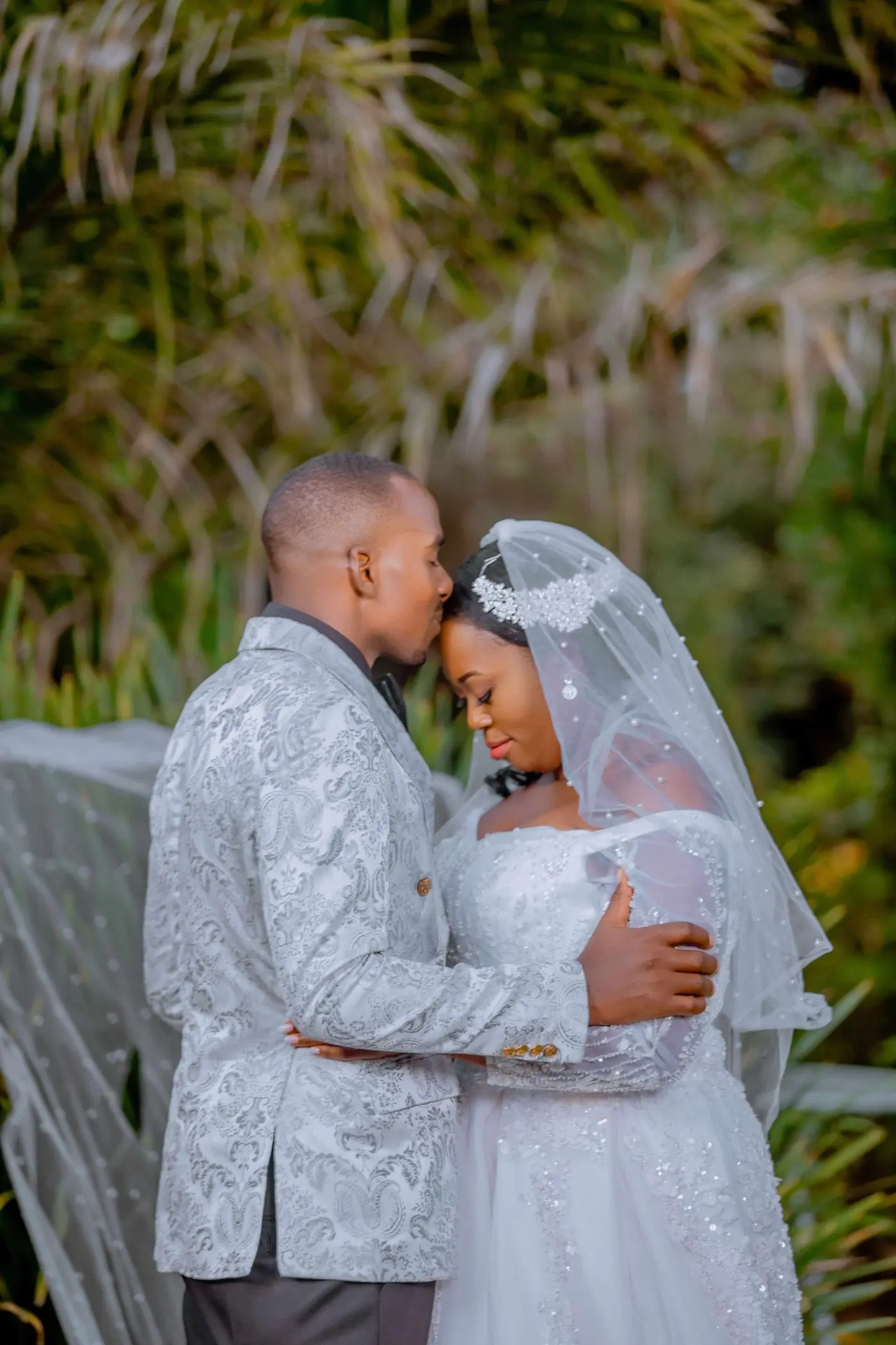 A groom kissing his bride on the forehead outdoors