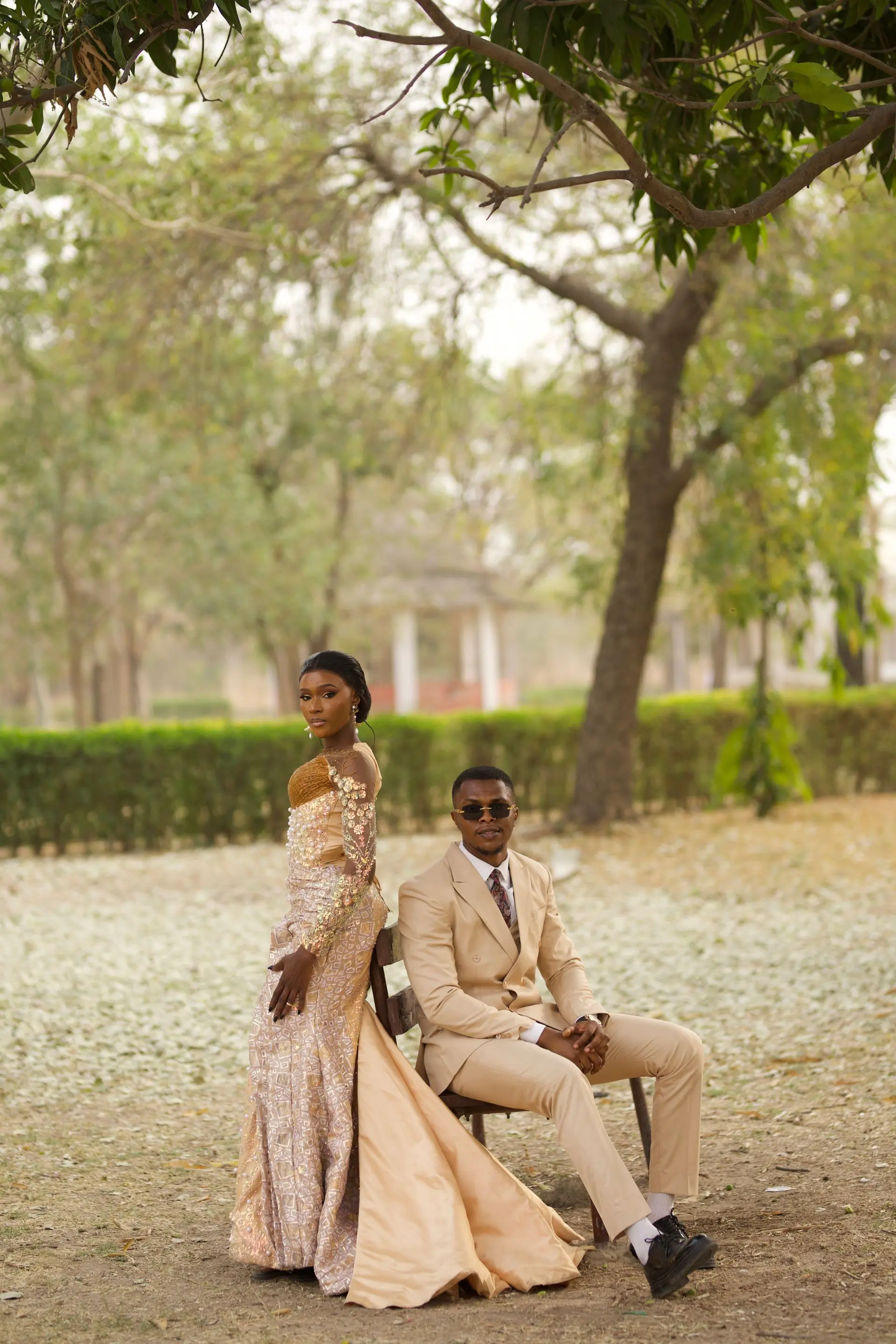 A couple in wedding clothes standing together on a lawn in front of a long hedge