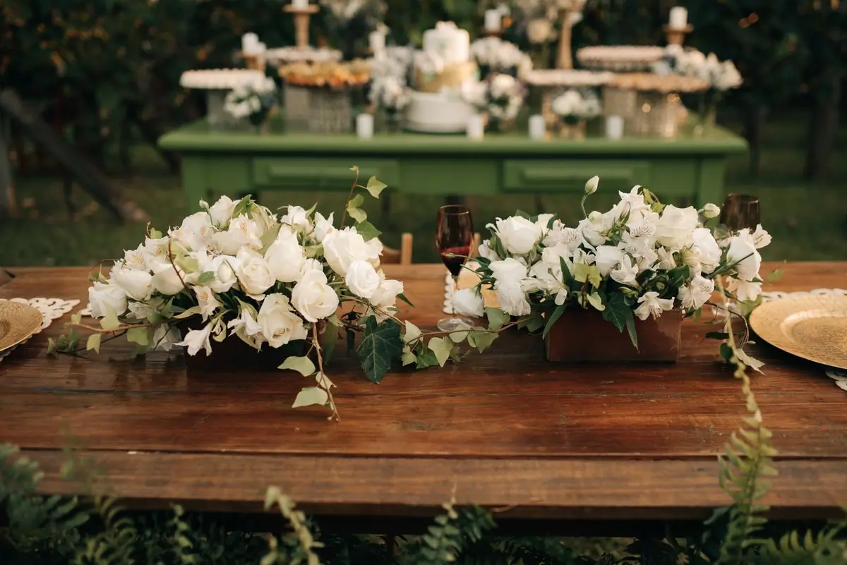 White roses arranged along a rustic wooden table outdoors