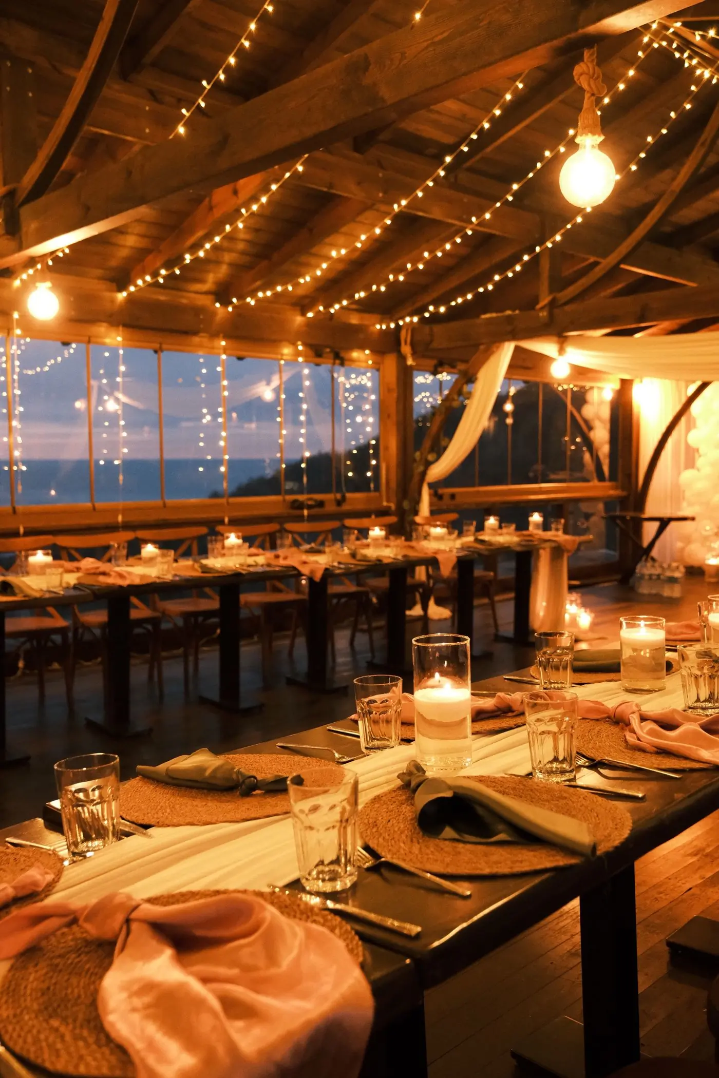 A long table set for dinner under warm hanging lights