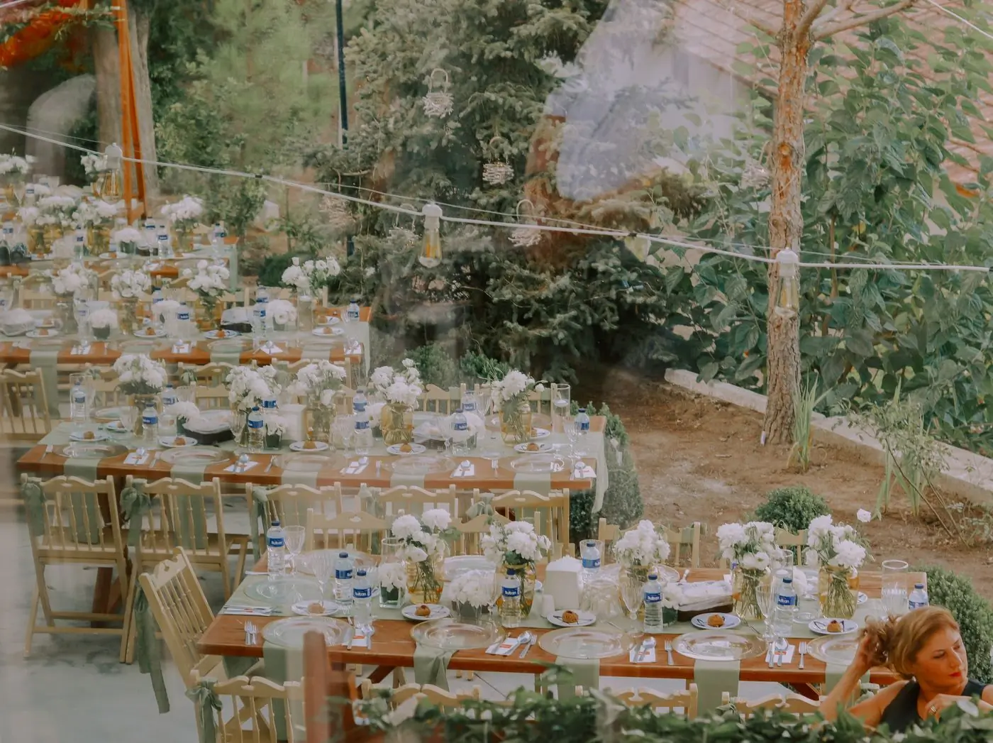 Rustic tables dressed with white flowers under trees at dusk