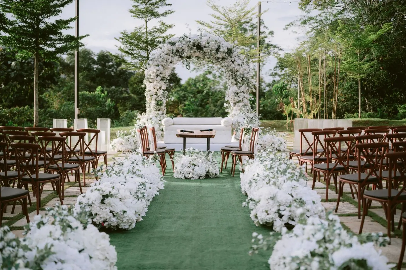 An outdoor ceremony set with a white floral arch and rows of chairs