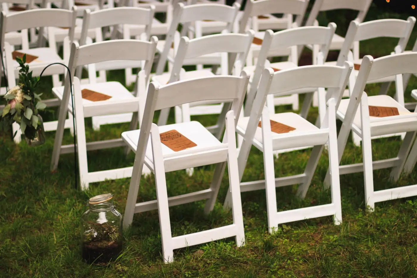 White folding chairs arranged in rows on a green lawn