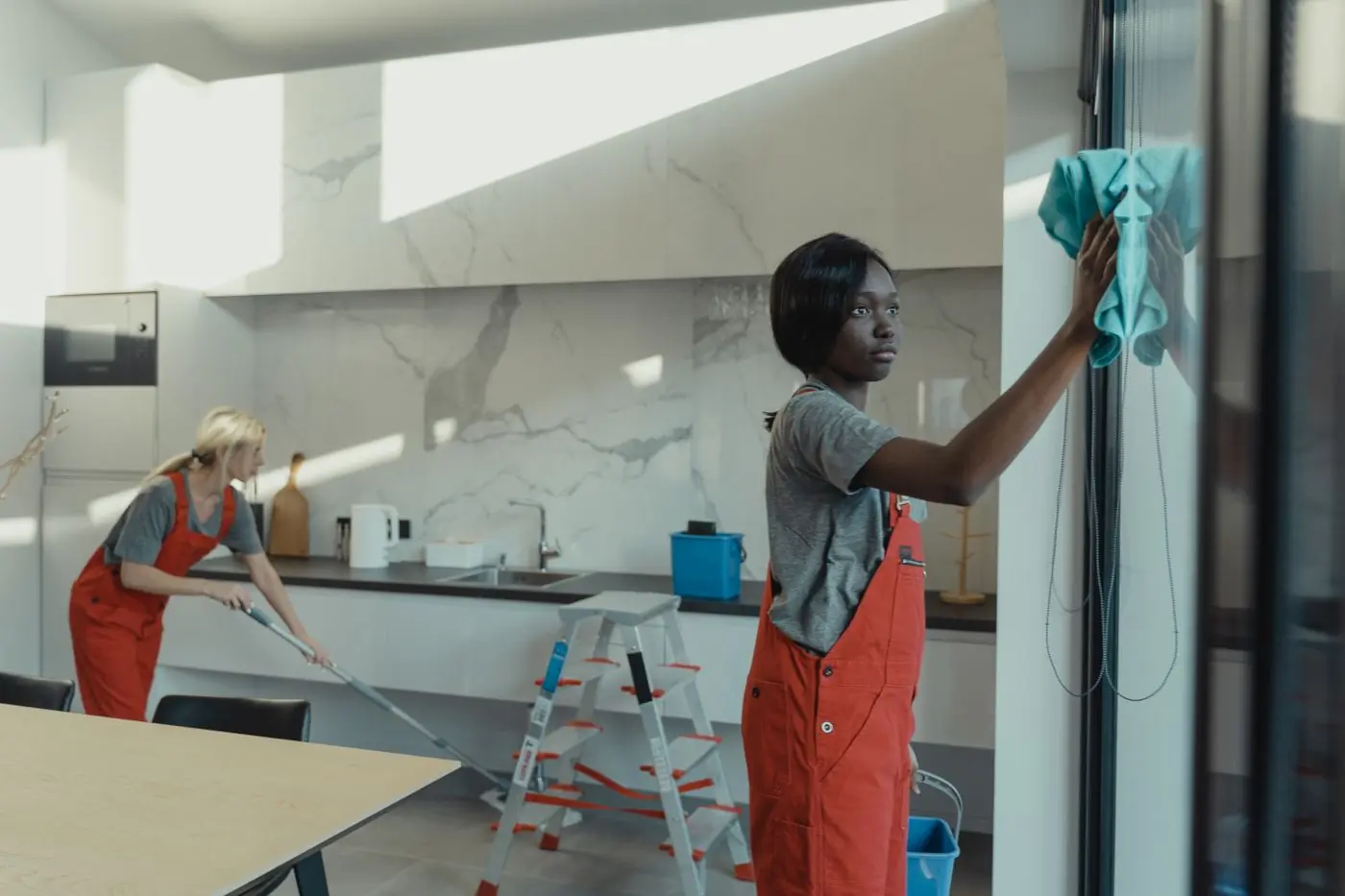 Two cleaners working through a bright open-plan kitchen