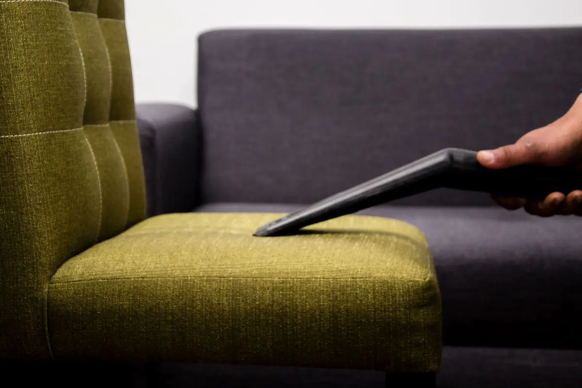 A vacuum nozzle lifting dust from an upholstered sofa cushion