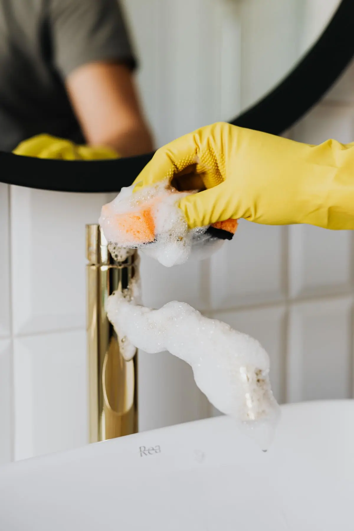 A gloved hand polishing a brass mixer tap