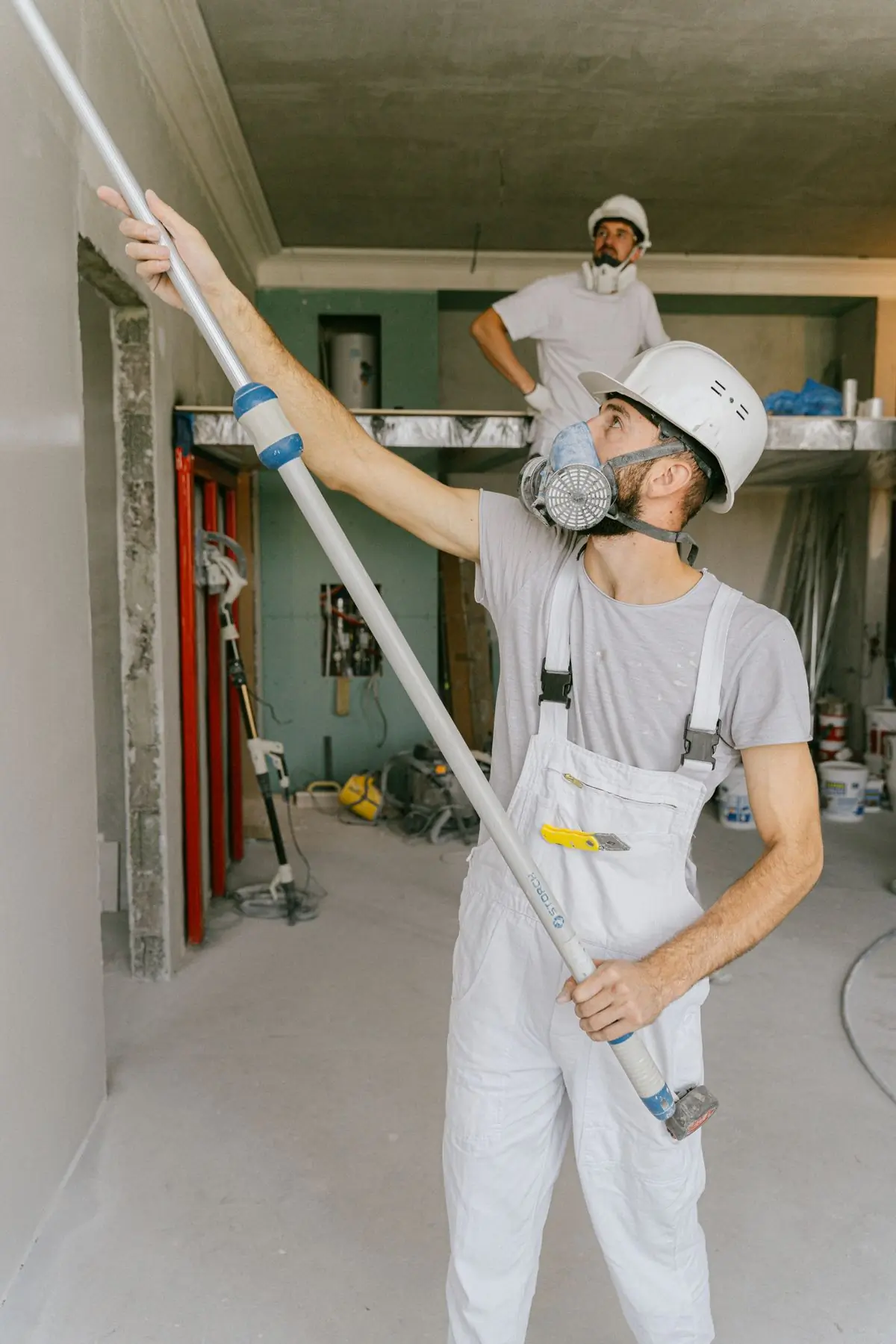 A decorator in a respirator rolling a primed commercial wall