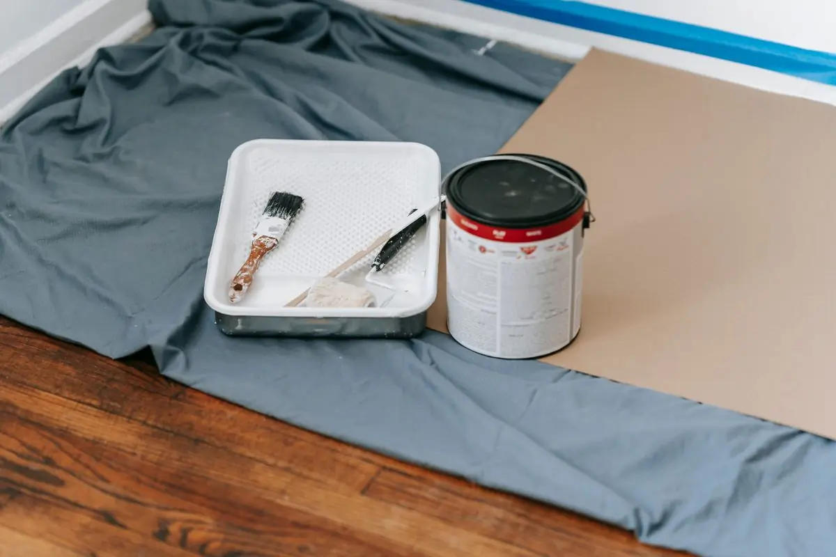 Brushes and an open tin standing on a dust sheet over a wooden floor