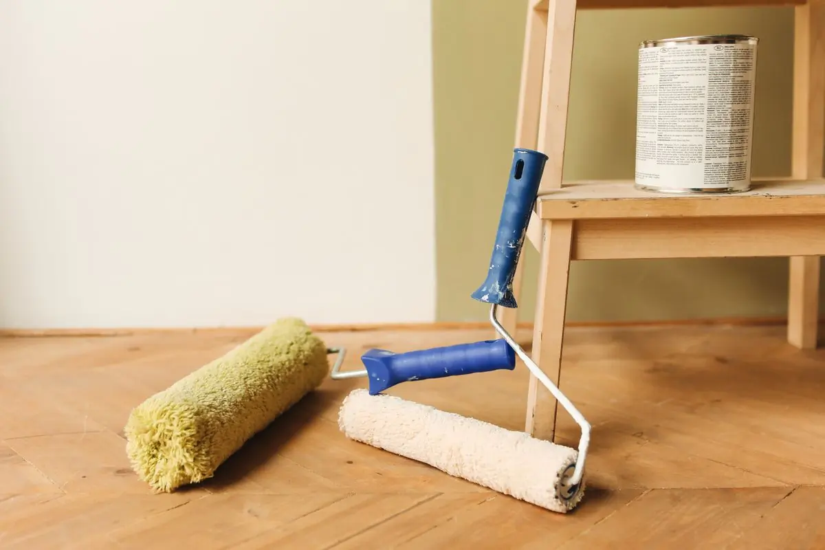 Two rollers and a tin left on a wooden floor beside a stepladder