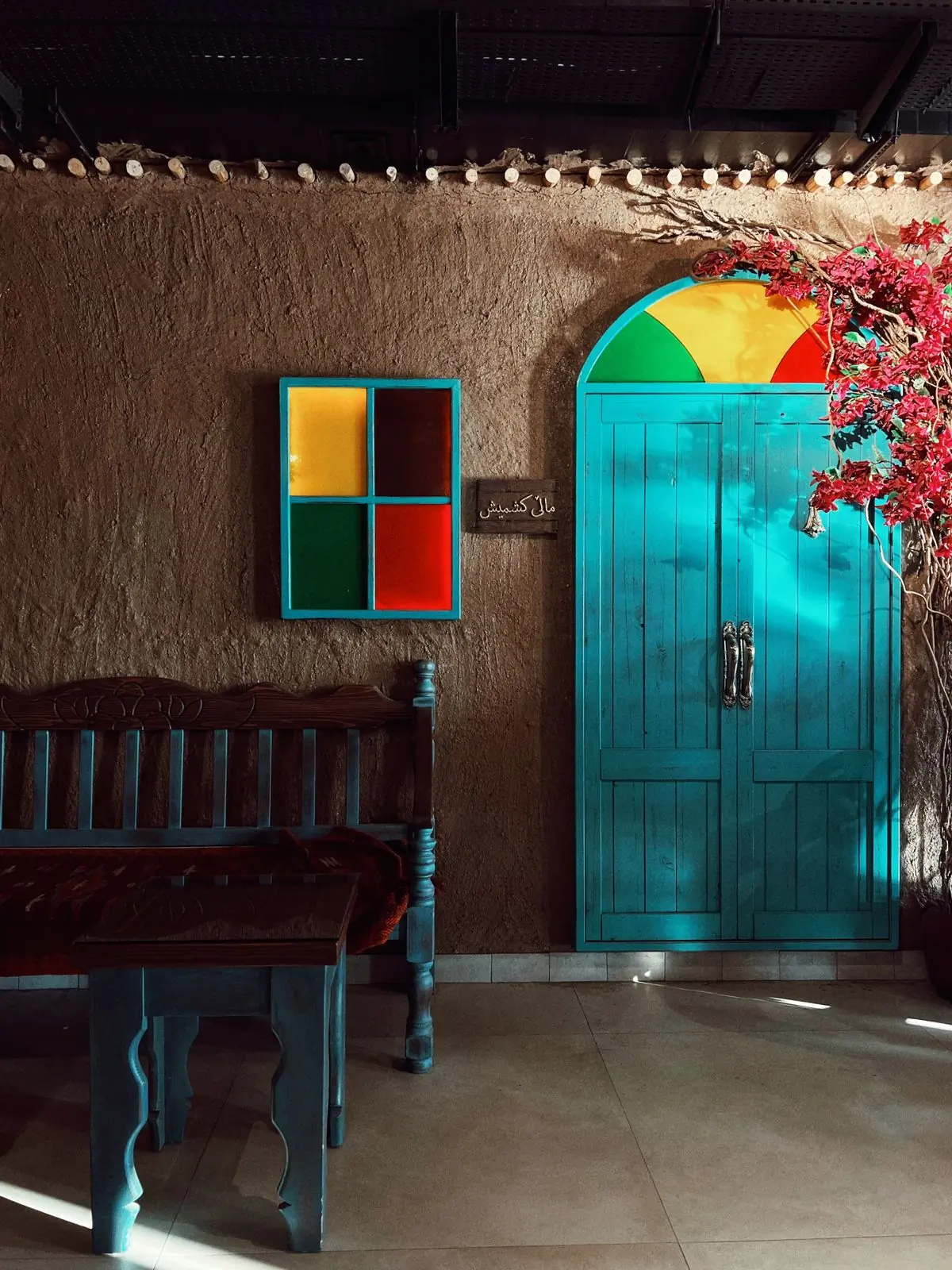 A teal painted door and a red-framed window on a rendered wall