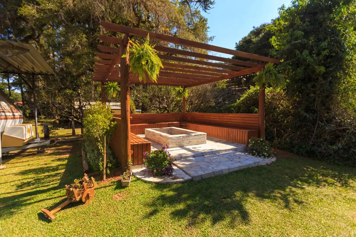 A timber pergola standing on a stone floor in a planted garden
