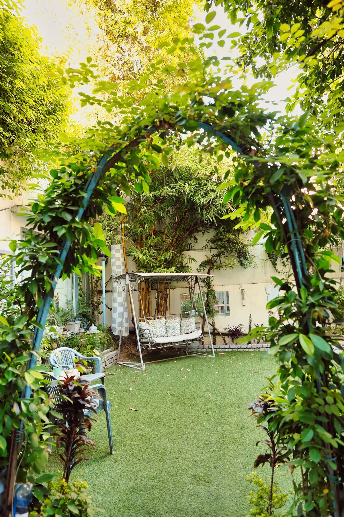 A garden swing under a leafy archway beside a house