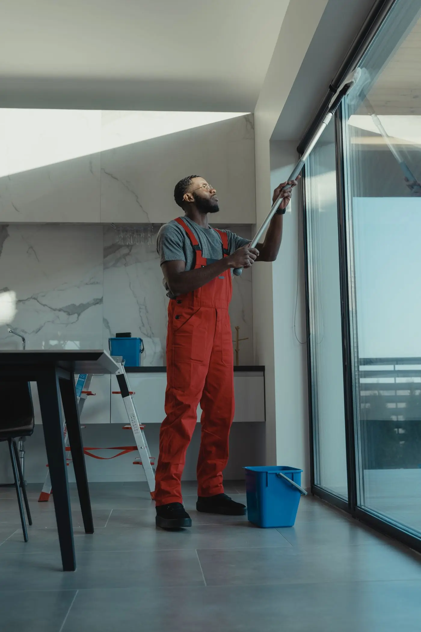A Handy tradesman cleaning a floor-to-ceiling window in a bright Accra apartment