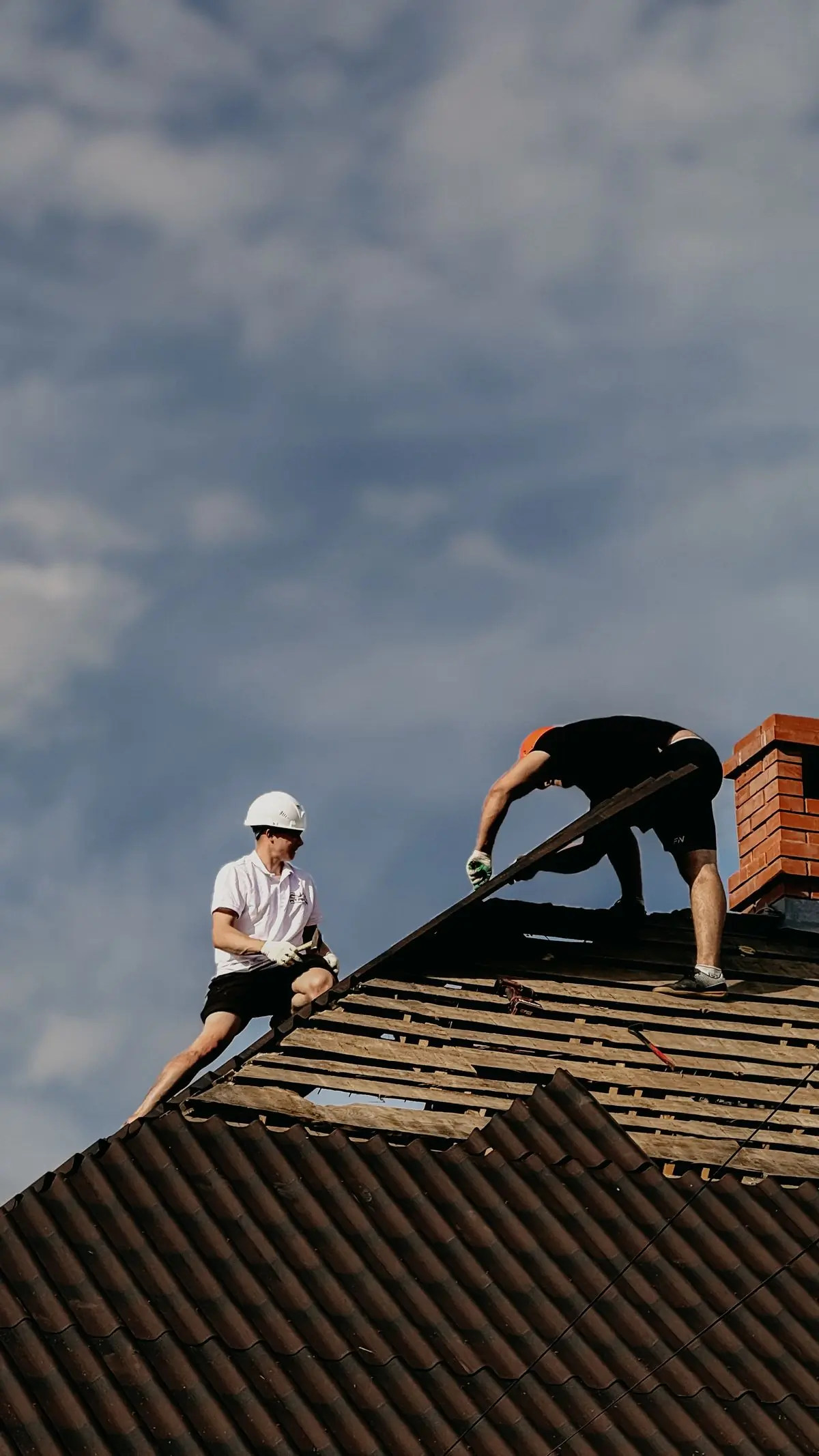 Two Handy roofers refastening sheeting on a pitched roof