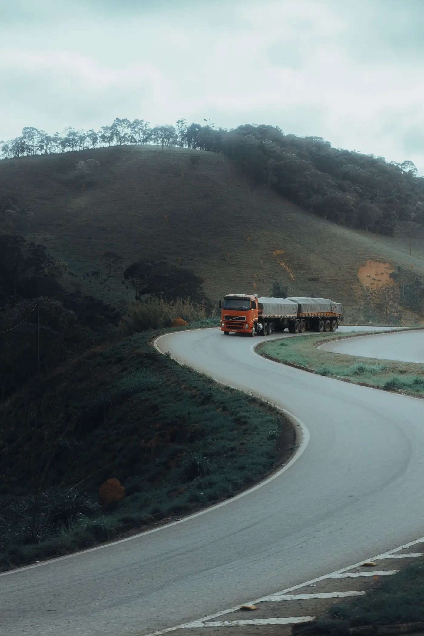 A lorry and trailer on a winding road through green hills