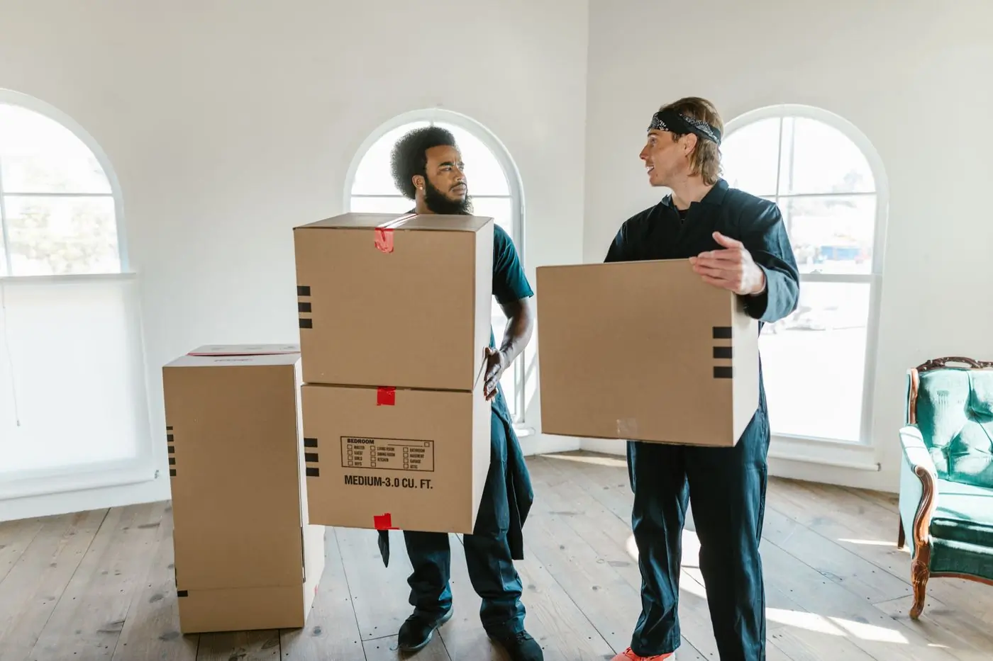 Two movers carrying labelled cartons through a bright empty room