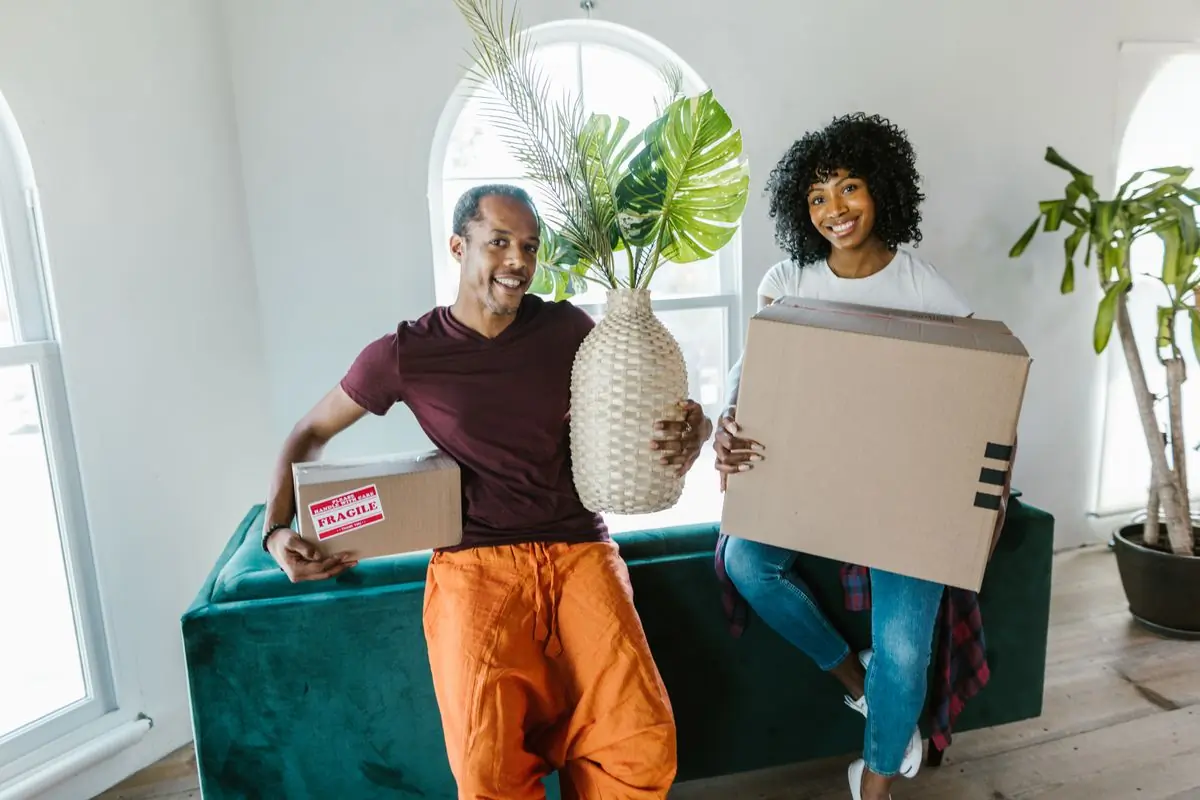 A couple carrying a carton and a plant into their new home