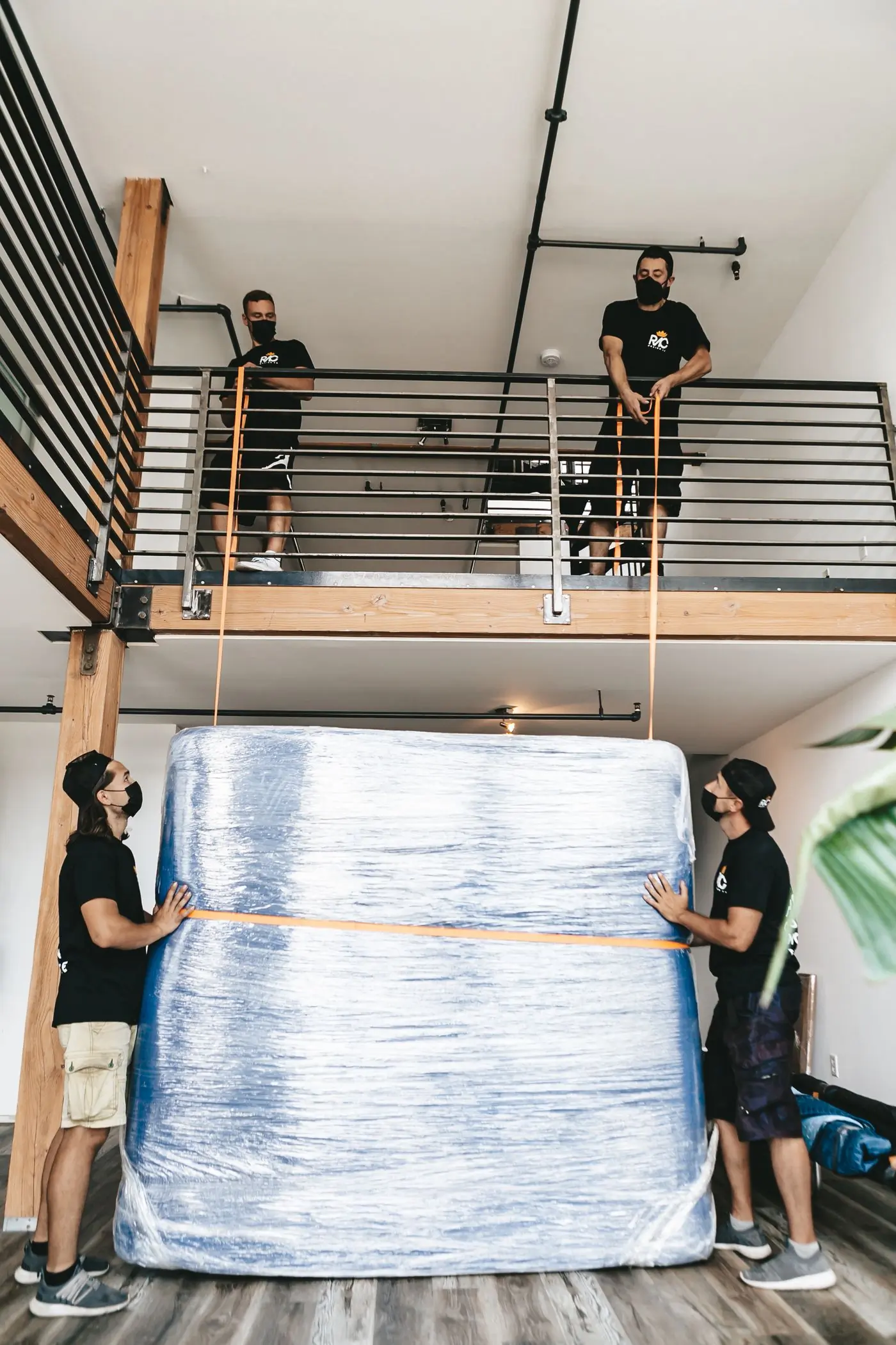 Four movers lifting a large wrapped item with straps
