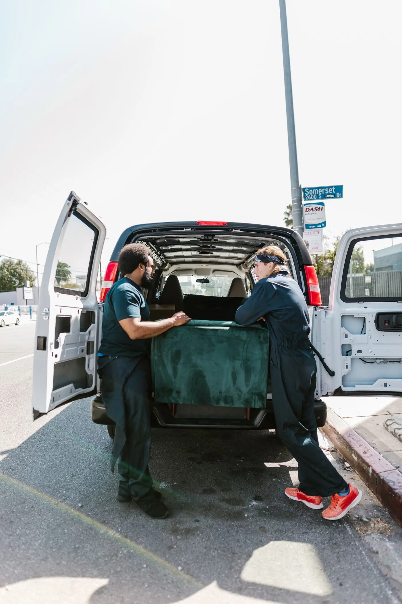 Two movers loading furniture into a van at the kerb