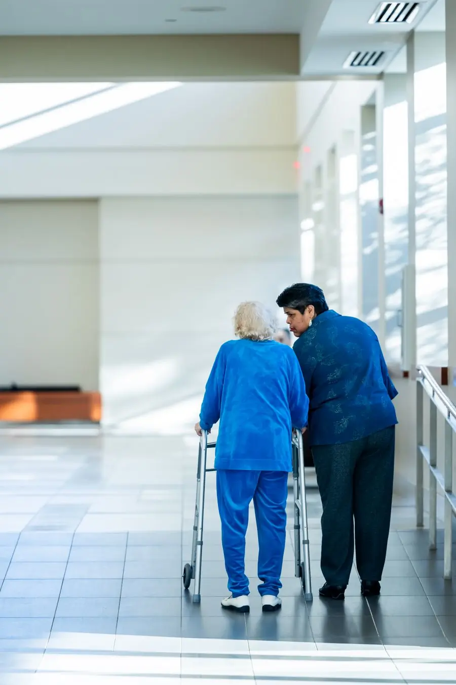 A nurse walking an older patient down the corridor with a frame