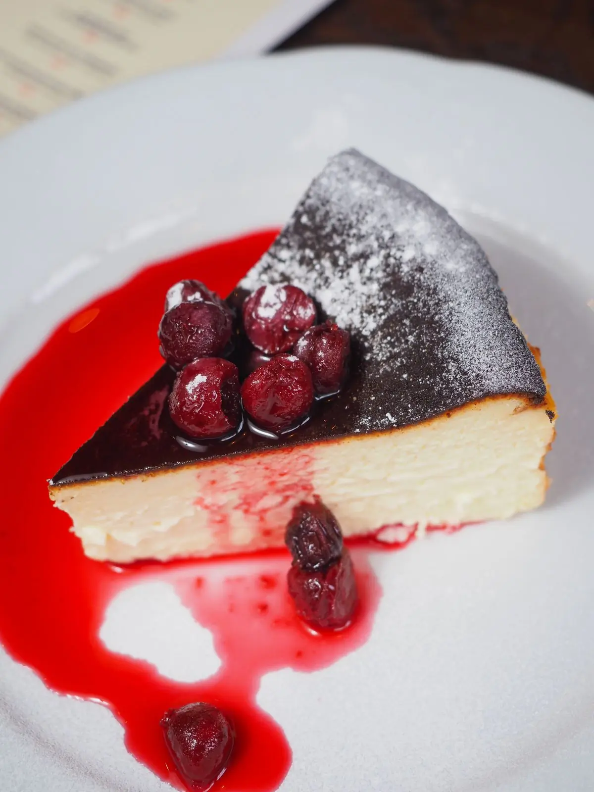 A slice of vanilla cheesecake with cherries on a white plate
