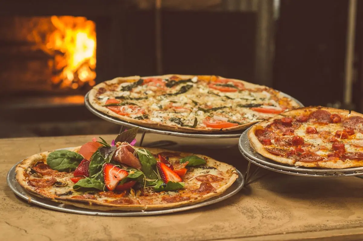 Three wood-fired pizzas beside the mouth of the oven