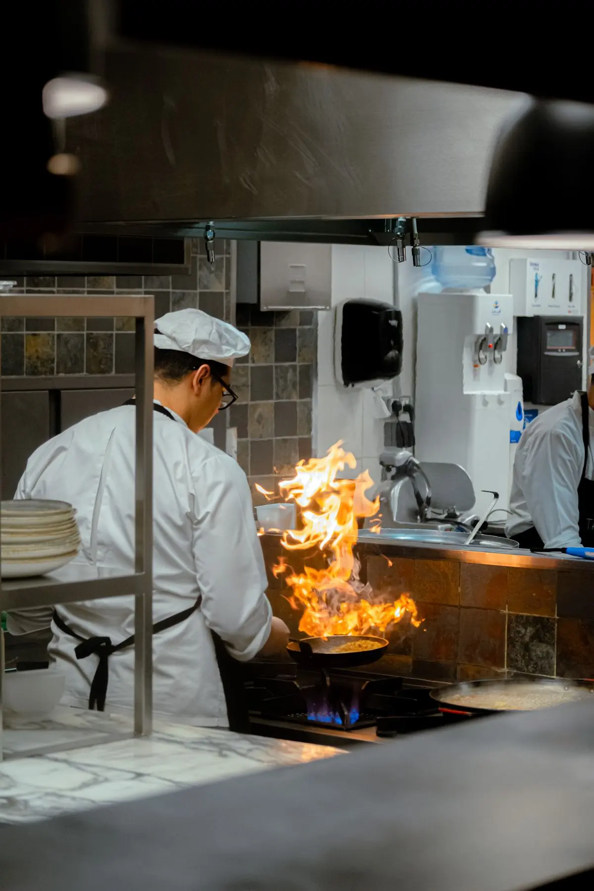 A cook working a flaming pan over the fire