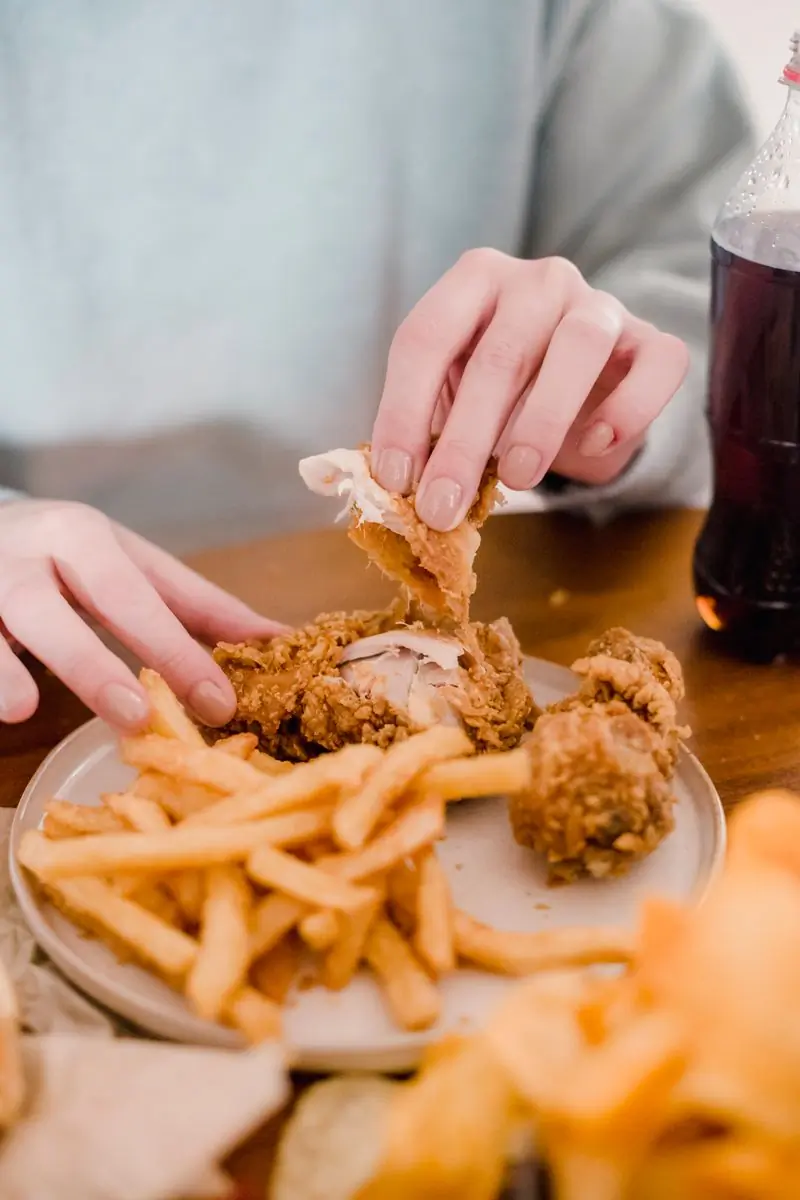 A hand reaching for fried chicken and fries