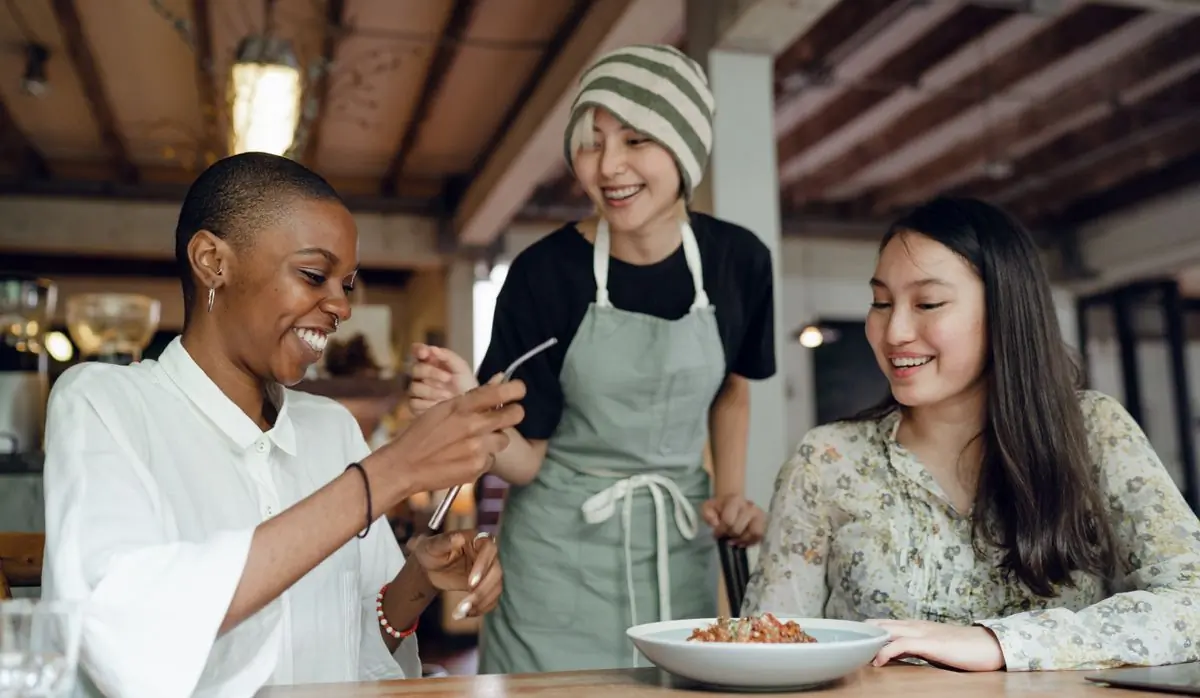 A server bringing a dish to two smiling guests