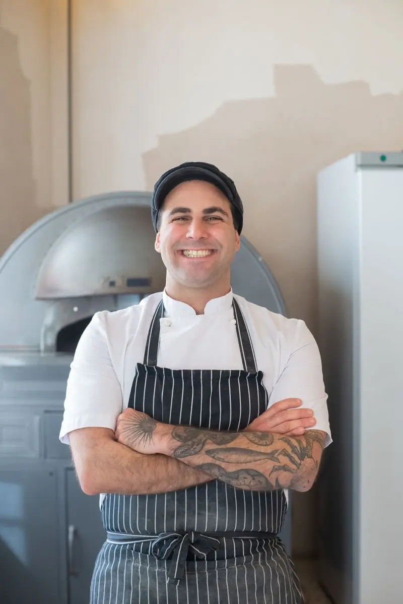 Tetteh Sowah in an apron beside the wood-fired oven