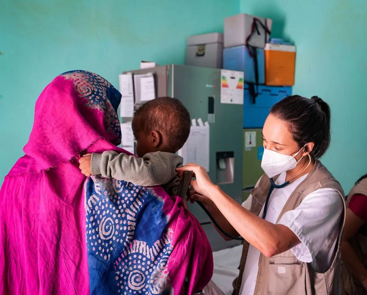 A clinician examining a small child held by their mother