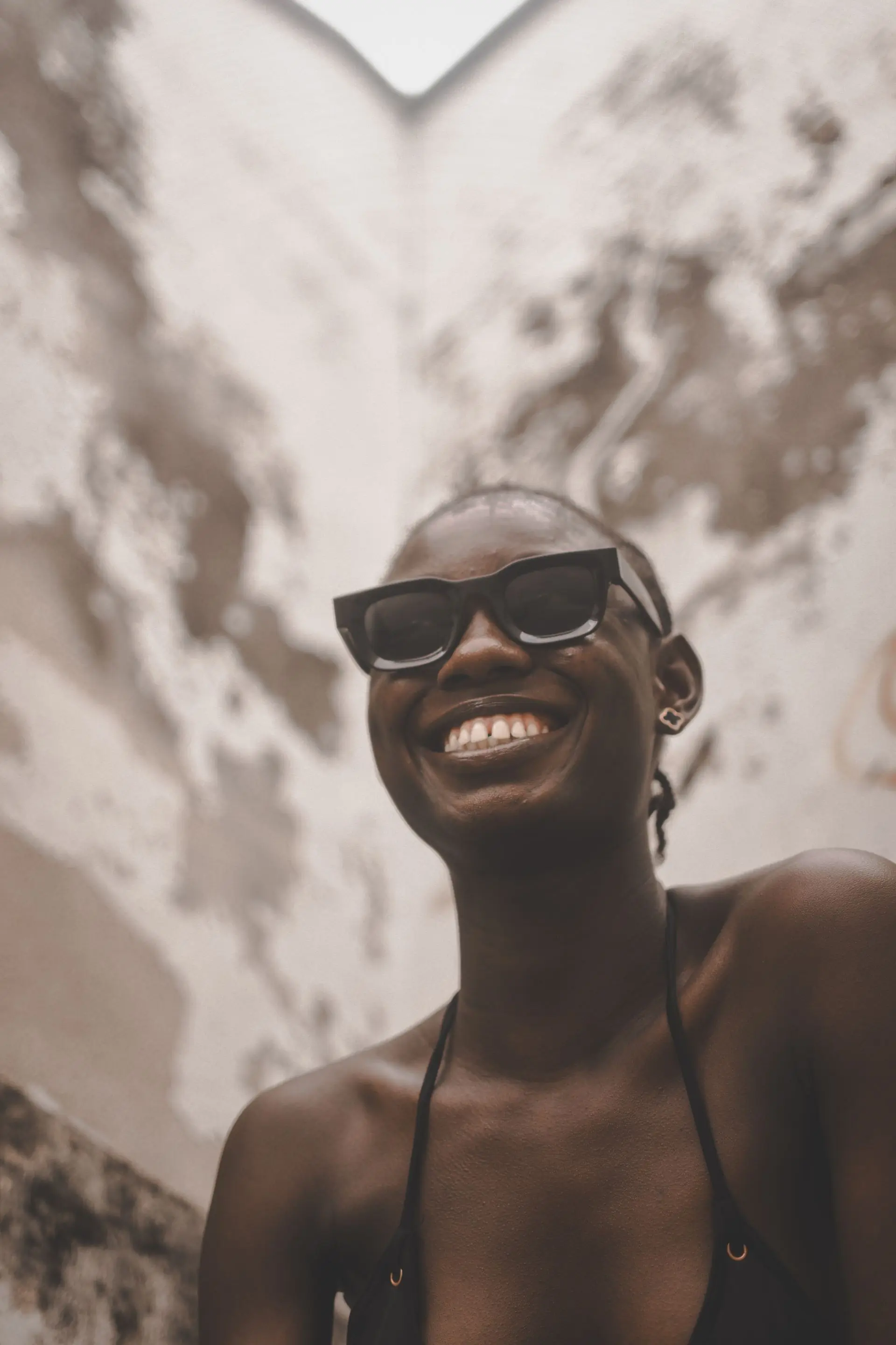 A person in sunglasses smiling in front of a sunlit wall