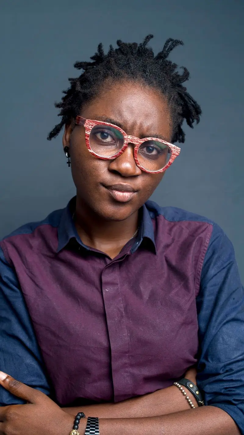 A woman in patterned optical frames against a plain wall