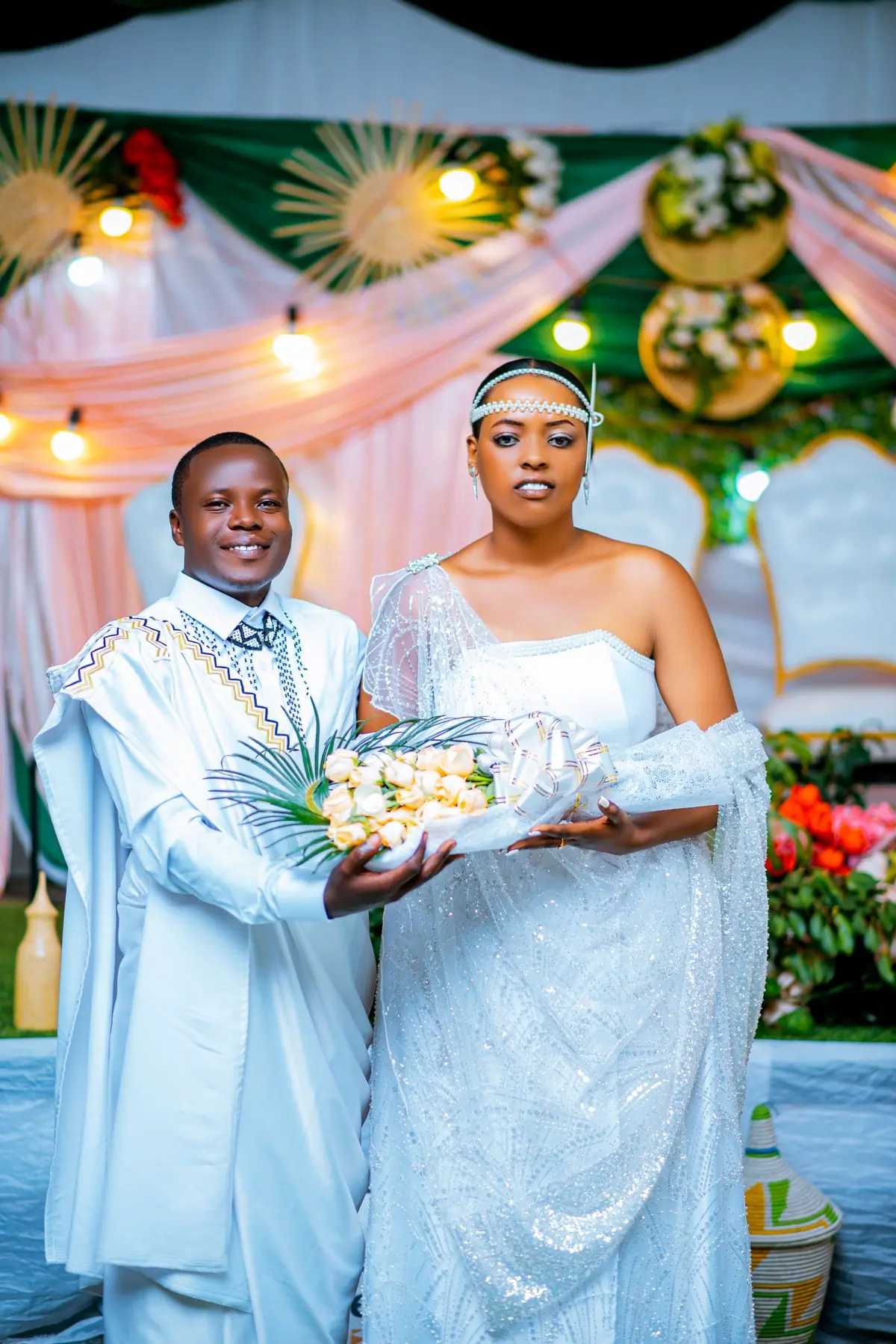 A couple in white and gold traditional dress holding a tray of flowers