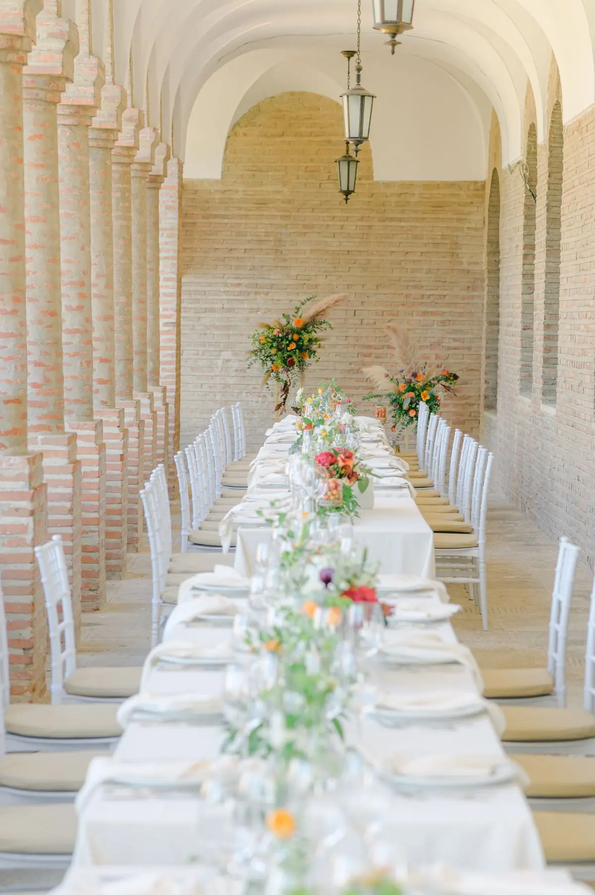 A long banquet table under a brick archway, dressed with pampas grass and candles