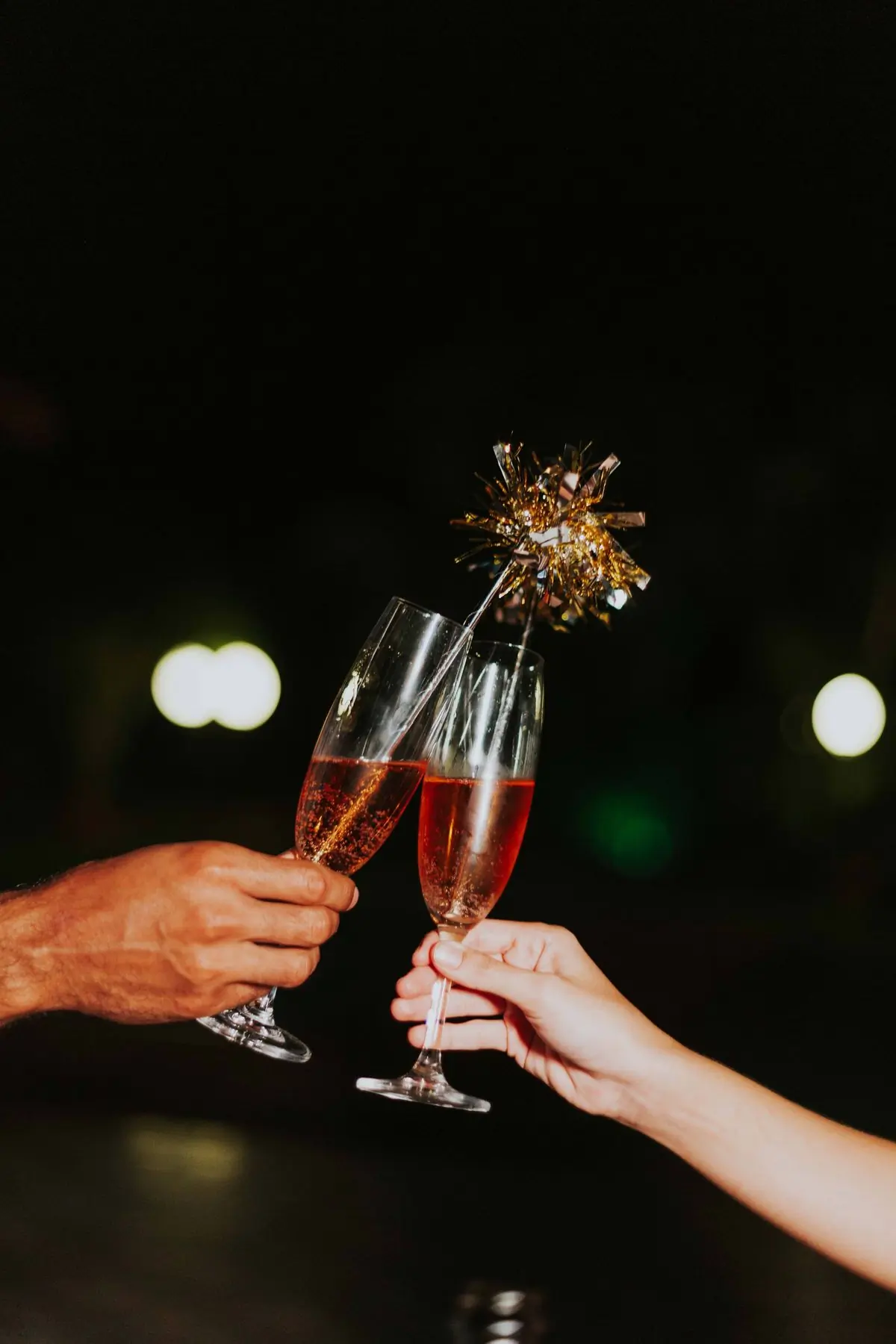 Two glasses of champagne touching, lit by a sparkler at night
