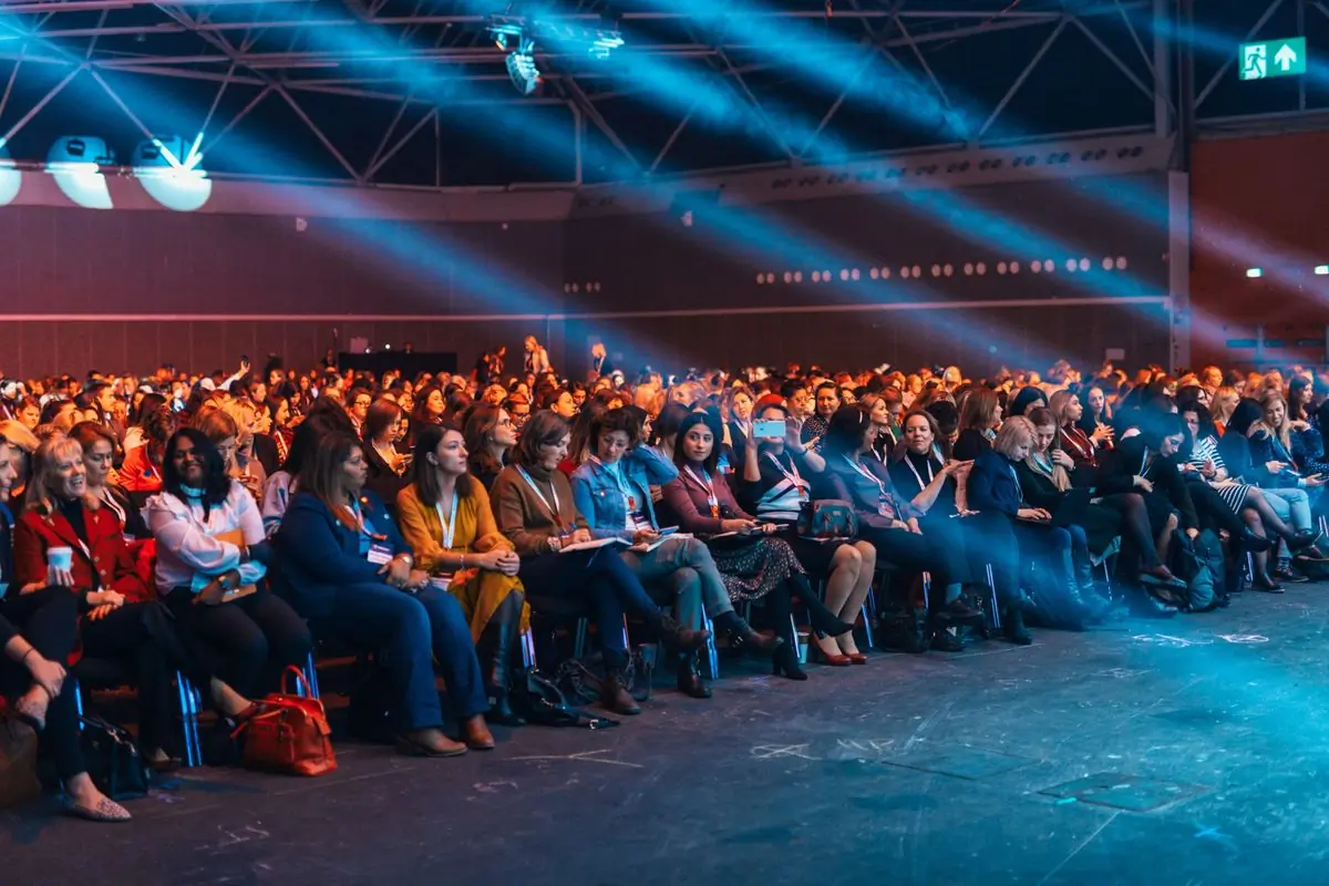 A full auditorium lit by blue stage beams during a conference