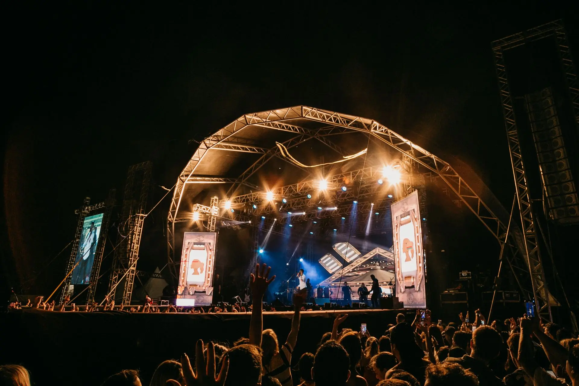 A crowd with their hands raised in front of an open-air stage lit up at night