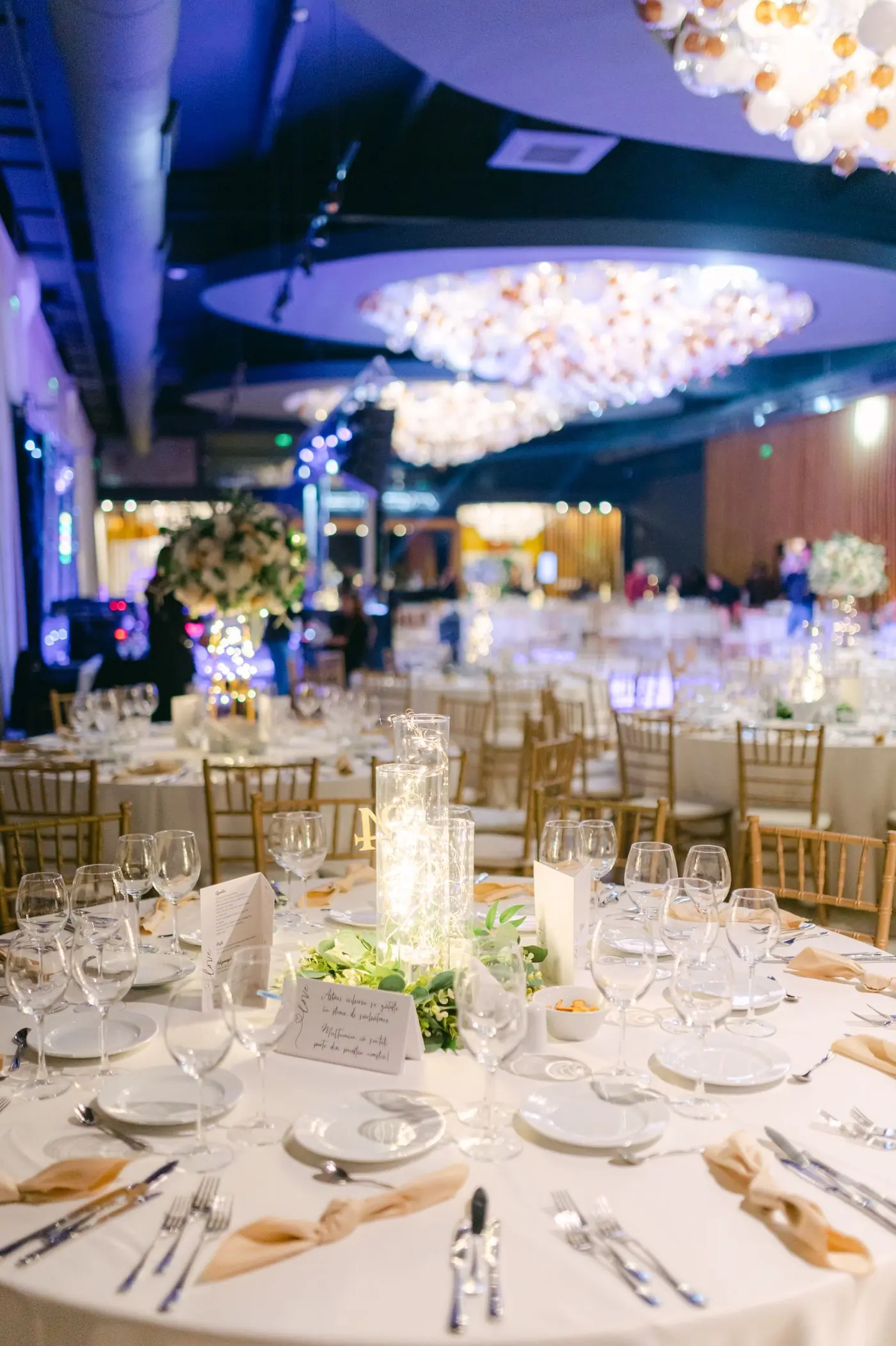 A ballroom laid for dinner under warm chandeliers and blue uplighting