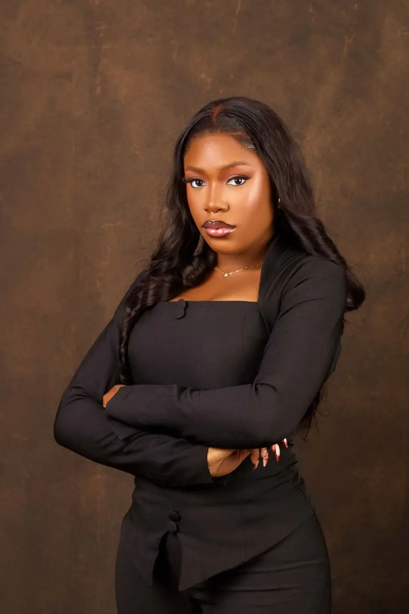 A woman in a black top standing with her arms folded against a warm brown backdrop