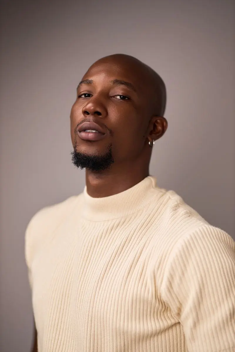 A man in a cream ribbed sweater against a soft grey studio backdrop