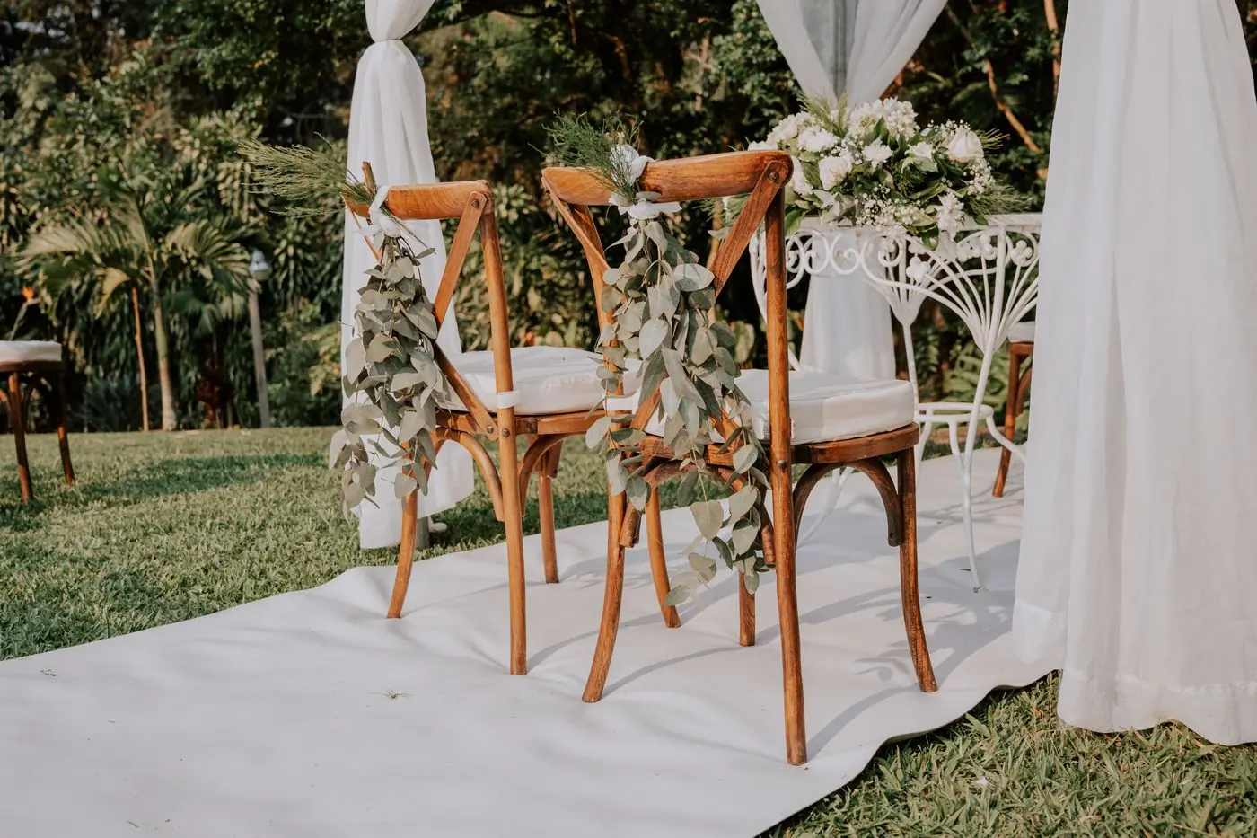 Two ceremony chairs dressed with eucalyptus under a draped canopy