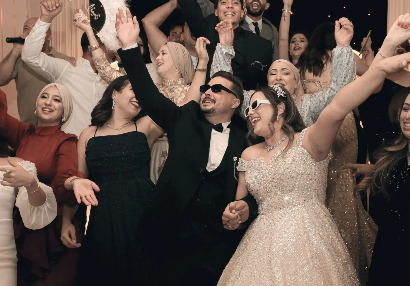 Guests in evening dress dancing with their arms raised at a reception