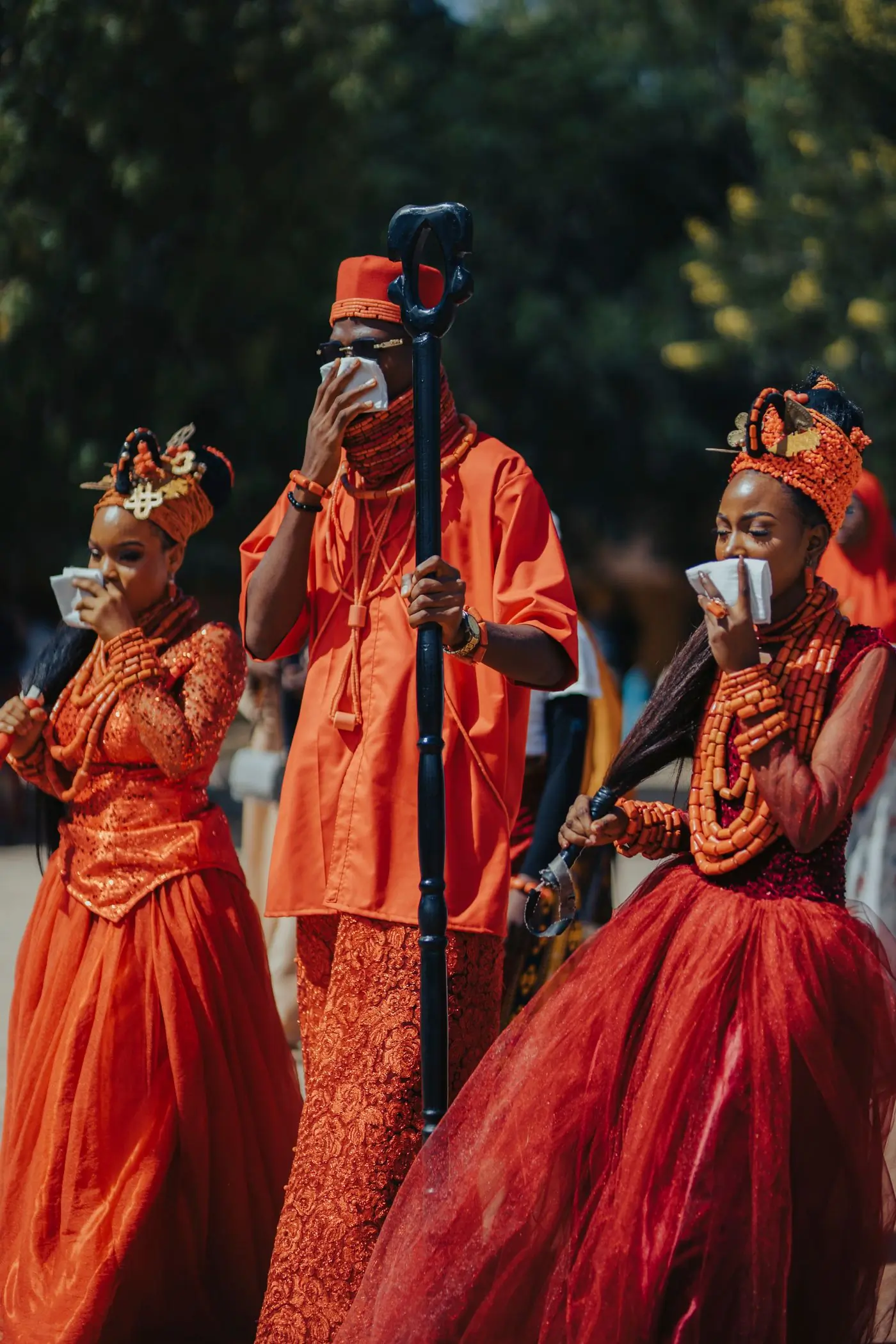 Three guests in vivid orange traditional dress at a customary ceremony