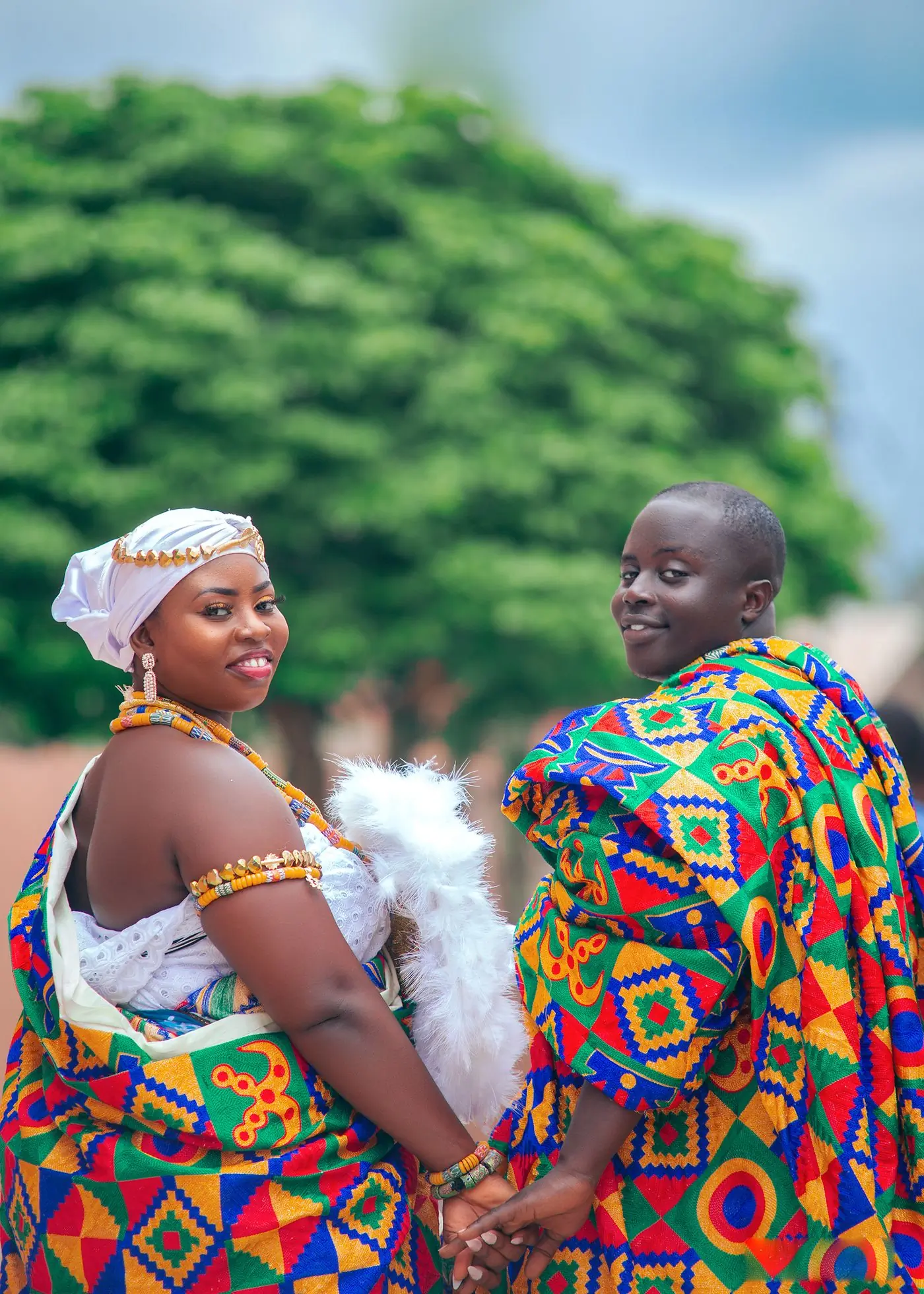 A couple in kente cloth laughing together outdoors