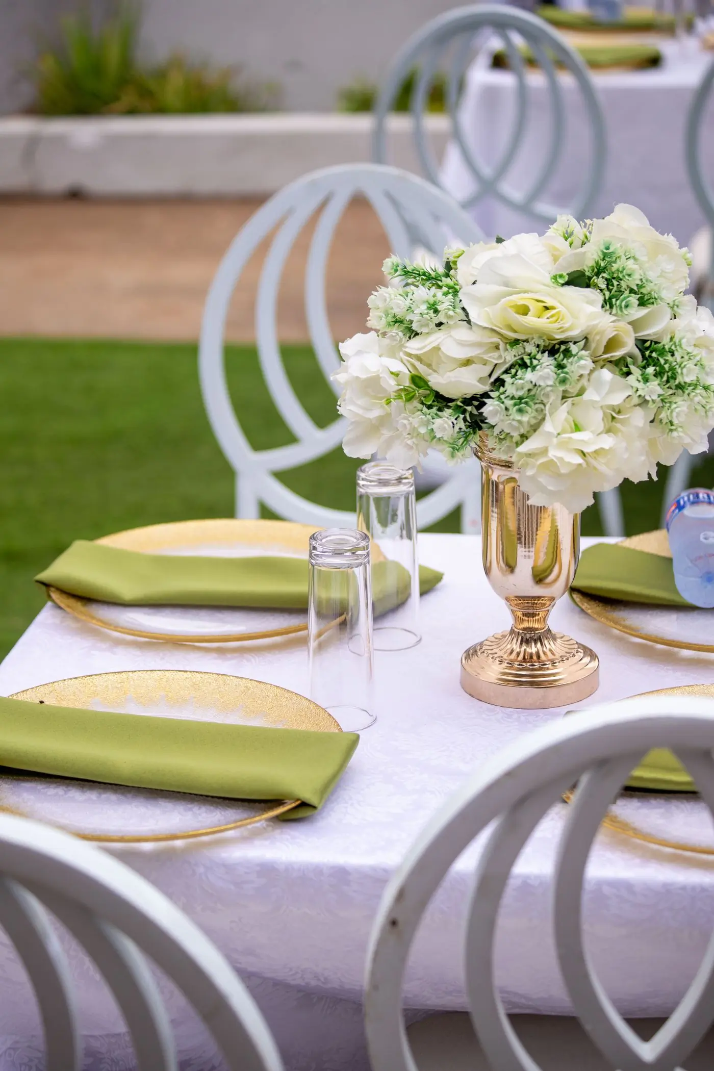 An outdoor table laid with white flowers, gold chargers and green napkins