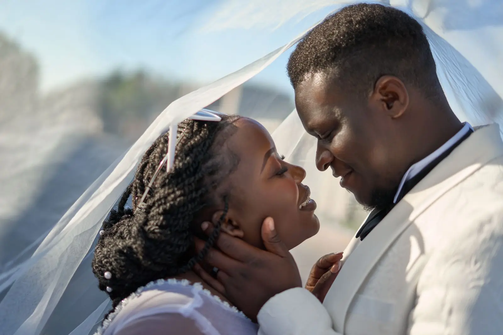A bride and groom under a lifted veil, close, in late afternoon light